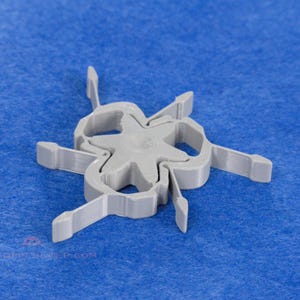 Pu&ograve; includere: Un oggetto di plastica grigia con un centro a forma di stella e sei bracci curvi, ciascuno con un'estremit&agrave; rettangolare. L'oggetto &egrave; posto su uno sfondo blu.