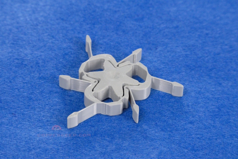 Pu&ograve; includere: Un oggetto di plastica grigia con un centro a forma di stella e sei bracci curvi, ciascuno con un'estremit&agrave; rettangolare. L'oggetto &egrave; posto su uno sfondo blu.