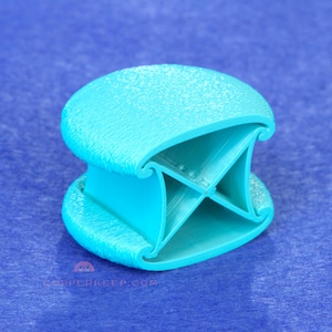 May include: A turquoise 3D-printed object with a textured surface. The object has a unique design with a rounded top and bottom connected by an X-shaped structure. The item is likely a decorative or functional piece.