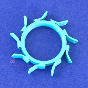 May include: A turquoise, circular object with a central hole and radiating, curved extensions. The object appears to be 3D-printed and has a textured surface. The background is a solid blue.