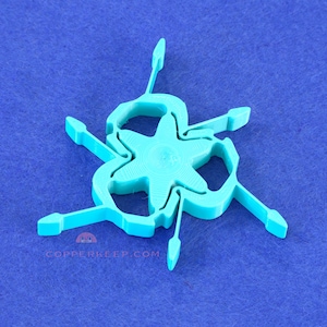 May include: A turquoise, star-shaped 3D-printed object with six curved arms extending outwards. The object is centered on a blue surface. The website address copperkeep.com is printed on the bottom left.