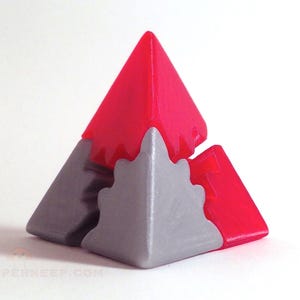 May include: A red and gray 3D puzzle in the shape of a pyramid. The puzzle is made up of three interlocking pieces.