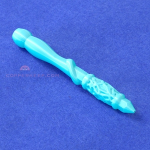 May include: A turquoise wand with a detailed handle and a faceted tip. The wand features a decorative, textured design on the handle and a smooth, rounded top. The wand is set against a blue background.