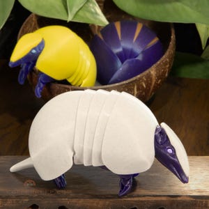 May include: Three small, segmented, animal-shaped toys. One is yellow, one is purple, and one is white with purple accents.