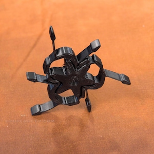 Pu&ograve; includere: Un oggetto nero a forma di stella con pi&ugrave; bracci e un design centrale. L'oggetto ha un aspetto tridimensionale ed &egrave; posto su uno sfondo marrone. Le braccia si estendono verso l'esterno, creando una forma geometrica unica.