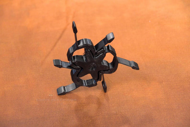 Pu&ograve; includere: Un oggetto nero a forma di stella con pi&ugrave; bracci e un design centrale. L'oggetto ha un aspetto tridimensionale ed &egrave; posto su uno sfondo marrone. Le braccia si estendono verso l'esterno, creando una forma geometrica unica.