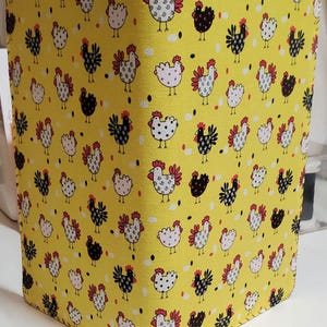 May include: A yellow fabric notebook cover with a repeating pattern of black and white chickens with red combs. The cover has a white polka dot pattern and is stitched around the edges.