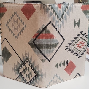 May include: A beige fabric notebook cover with a geometric pattern in shades of red, green, and blue. The pattern features diamonds, triangles, and zigzags.