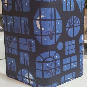 May include: A black fabric notebook cover with a repeating pattern of blue windows with stars, moons, and plants. The windows are different shapes and sizes.