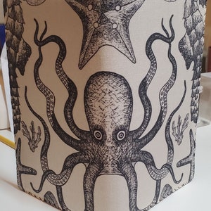 May include: A beige fabric notebook cover with a black and white illustration of an octopus, starfish, and other sea creatures.