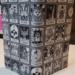 May include: Black and white fabric with a repeating pattern of tarot cards. The cards are arranged in a grid and feature various symbols and imagery, including the sun, moon, stars, and a skull.