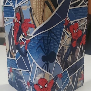 May include: A blue and white fabric with a repeating pattern of Spiderman in different poses. The fabric features a blue background with white spiderwebs and cityscapes.