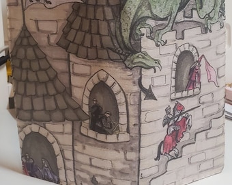 May include: A fabric book cover with a watercolor illustration of a castle with a dragon on top. The castle has a brown roof and brick walls. There are windows with people looking out of them. A knight on a horse is climbing the stairs to the castle.