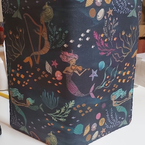 May include: A black fabric pouch with a colorful mermaid pattern. The pattern features mermaids playing musical instruments, seashells, and fish. The pouch has a stitched edge.