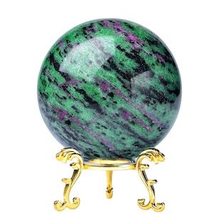 Peut inclure: Une sphère de pierre précieuse verte, noire et violette sur un support doré. La sphère est polie et présente un motif tourbillonnant.