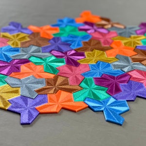 May include: A colorful geometric puzzle made of interlocking pieces in various shades of blue, green, purple, orange, gold, and silver. The pieces are arranged in a pattern that resembles a honeycomb.