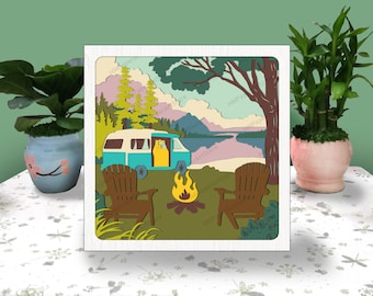 May include: A papercraft scene of a vintage camper van parked in a forest clearing by a lake. The camper is blue and white with a yellow propane tank. Two brown wooden chairs are placed in front of a campfire. The scene is surrounded by green trees and a mountain range in the background.