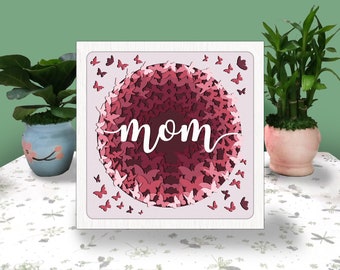 以下が含まれることがあります： 白地にピンクと白の蝶の円が描かれたカードで、中央に「mom」の文字が書かれています。