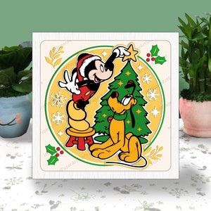 Puede incluir: Ilustración navideña con Mickey Mouse colocando una estrella en un árbol de Navidad verde, con Pluto observando. El diseño incluye copos de nieve y acebo, dentro de un marco circular amarillo y crema.