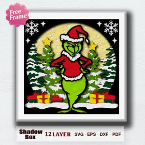 Pode incluir: Uma caixa de sombra emoldurada com um personagem de desenho animado verde em um traje e chapéu de Papai Noel vermelhos, com acabamento branco. O fundo inclui árvores de Natal, estrelas amarelas e presentes. O texto "Shadow Box" e "12 LAYER SVG EPS DXX PDF" está na parte inferior.