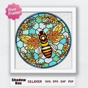 May include: A framed shadow box design featuring a detailed bee illustration. The bee is centered within a circular stained-glass style design with yellow, orange, and black colors. The background includes a honeycomb pattern and floral accents. The frame is white, and the design is labeled as 10 layer SVG, EPS, DXF, and PDF.