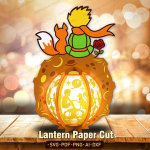 May include: A layered paper cut lantern featuring a design of the Little Prince with a fox, a rose, and a planet. The lantern is orange and yellow with intricate cut-out details. The text "Lantern Paper Cut" is at the bottom.