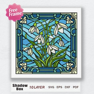 May include: A stained glass design featuring a bouquet of white snowdrop flowers with green leaves against a blue and green background. The design is framed in a decorative border.