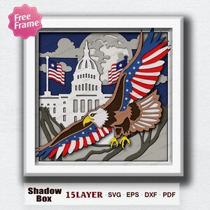 May include: A layered paper shadow box art piece featuring an American bald eagle in flight with outstretched wings. The eagle is set against a backdrop of the U.S. Capitol building, American flags, and a blue sky. The words "Shadow Box" and "15 LAYER" are at the bottom.