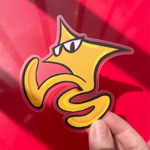May include: A yellow star-shaped sticker with a black outline, featuring a cartoon character wearing black sunglasses. The character has a pointed top, a long curved arm, and a winding, snake-like lower body section in a vibrant yellow hue.