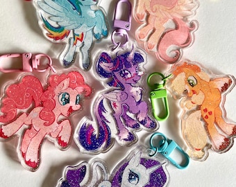 May include: Collection of colorful acrylic keychains featuring cartoon pony characters. Each keychain has a unique design with glitter accents and a metal clasp in various colors, including red, pink, yellow, and blue.