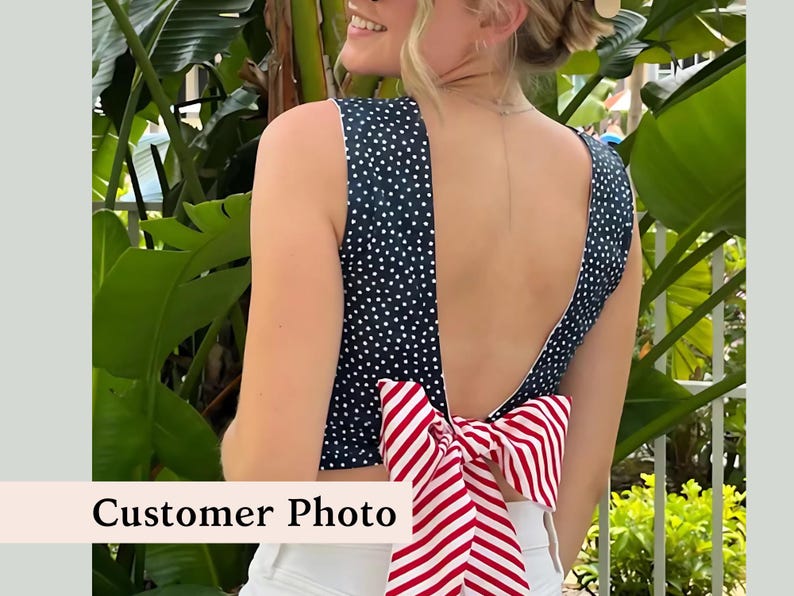May include: A navy blue and white polka dot sleeveless top with a red and white striped bow tied at the back.