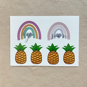 May include: A sheet of stickers with four pineapple designs and two rainbow designs. The rainbows are in shades of purple, pink, and orange. The rainbows have the words "hope" and "soon" written on them.