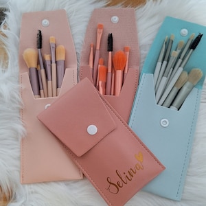 Könnte beinhalten: Drei Make-up-Pinselhalter mit verschiedenen Farben aus Kunstleder. Die Halter sind geöffnet und mit Make-up-Pinseln gefüllt. Ein Halter ist rosa und hat den Namen "Selina" in goldenen Buchstaben darauf.