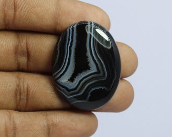 May include: Black and white agate cabochon with a smooth, polished surface. The stone has a swirling pattern of white lines on a black background.