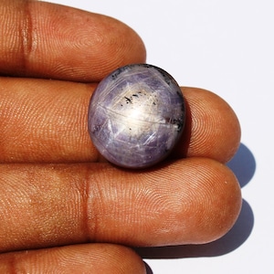 May include: A round, purple star sapphire gemstone with a silver sheen. The gemstone is approximately 2.5 cm in diameter.