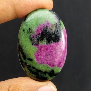 Peut inclure: Pierre précieuse de forme ovale, présentant un mélange de couleurs vives. La pierre affiche un mélange saisissant de magenta profond, de vert luxuriant et d'inclusions noires. La surface polie met en valeur les motifs et textures naturels du minéral.