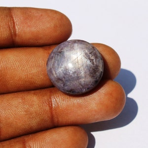 Op de afbeelding: Een ronde, grijze edelsteen met een stervormig patroon. De edelsteen is gezet in een zilveren ring.