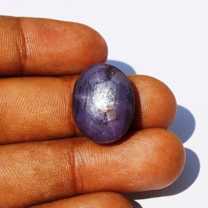 May include: A purple oval-shaped gemstone with a star-like pattern in the centre. The gemstone is set in a silver ring.