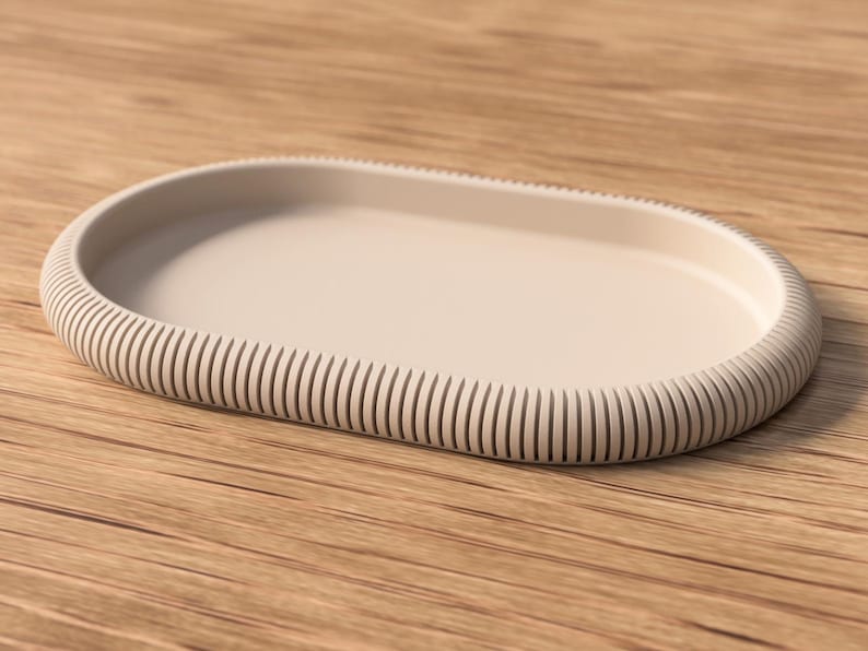 May include: A beige, oval-shaped tray with a ribbed edge. The tray is made of a solid material and sits on a wooden surface. The design is minimalist and modern, suitable for home decor or serving.