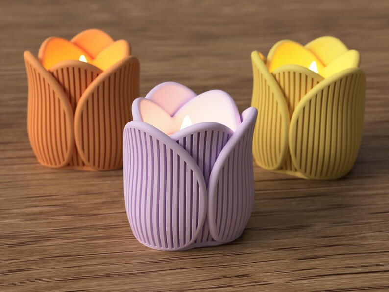 May include: Three tulip-shaped candle holders in orange, lavender, and yellow, each with a lit candle inside. The holders have vertical ribbed detailing and sit on a wooden surface. The candles emit a warm, inviting glow.
