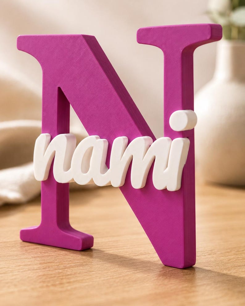 May include: A large, magenta-colored capital letter N made of a solid material. Attached to the front of the letter is the name nami written in white, lowercase, cursive-style letters. The object has a smooth, matte finish and stands upright.