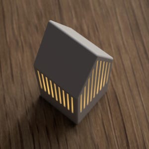 May include: A gray, house-shaped decorative lamp with vertical, golden-yellow light slits. The lamp is on a wooden surface. The lamp's design is modern and minimalist, suitable for home decor.