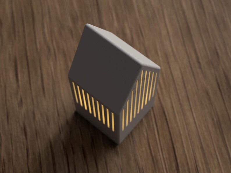 May include: A gray, house-shaped decorative lamp with vertical, golden-yellow light slits. The lamp is on a wooden surface. The lamp's design is modern and minimalist, suitable for home decor.