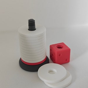 May include: A white and red stacking tower with a black base and a black screw on top. There are two white rings next to the tower and a red cube with black dots.