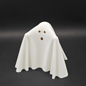 Puede incluir: Figurita de fantasma blanco con una cara simple, dos ojos y una boca, hecha de un material blanco liso.