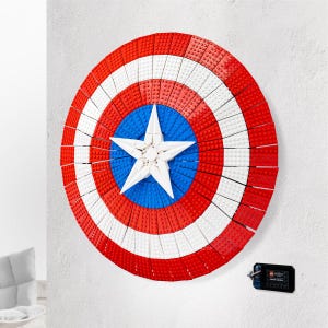May include: A large, circular shield constructed from red, white, and blue building blocks. The shield features concentric rings of red and white, a blue center with a white star, and is mounted on a white wall. A small black accessory is visible.