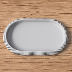 May include: A light gray, oval-shaped serving tray with a textured, ridged border. The tray is set against a warm, wooden background. The design is simple and elegant, suitable for serving food or displaying items.