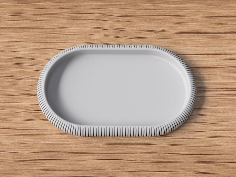 May include: A light gray, oval-shaped serving tray with a textured, ridged border. The tray is set against a warm, wooden background. The design is simple and elegant, suitable for serving food or displaying items.