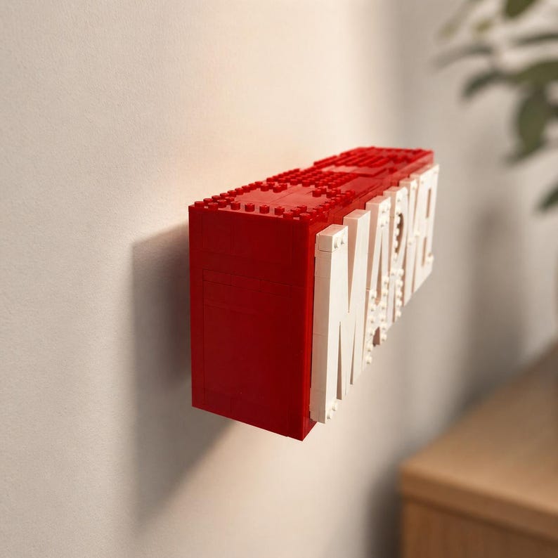 May include: A red and white LEGO-style sign featuring the word "MARVEL". The sign is constructed from red bricks with the white letters attached to the side. The sign is mounted on a white wall.