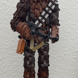 May include: A Lego sculpture of Chewbacca from Star Wars, constructed from various shades of brown Lego bricks. The figure holds a black weapon and has a bandolier. The base includes a character profile and the Star Wars logo.
